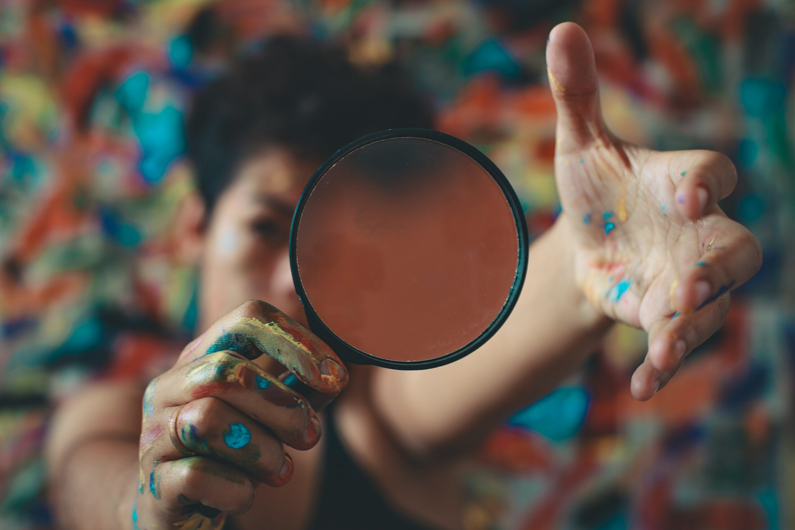 woman in front of a painting holding a magnifying glass with paint on her hands