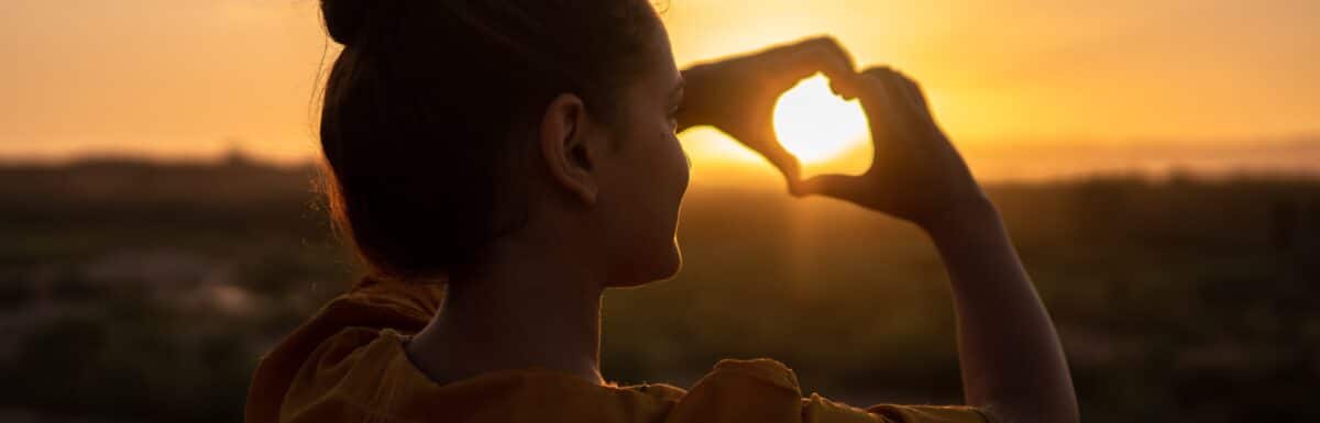 woman making a hear with her hands during sunrise